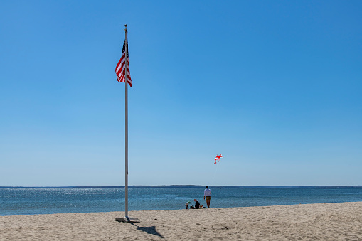 Old Greenwich, CT, USA-May 2022; Panoramic view of beach at Greenwich Point Park or Tods Point with American flag and family and children having fun and flying a kite with Long Island Sound in back