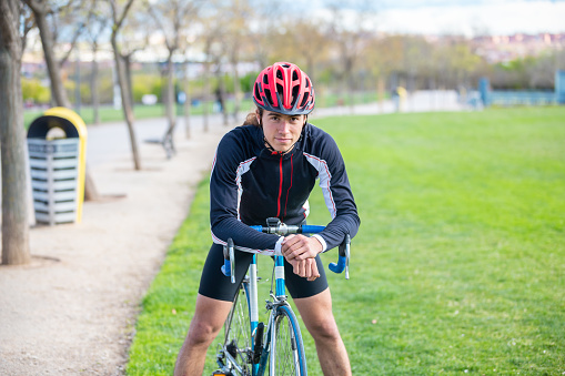 Smiling young fit male cyclist in sportswear and helmet sitting on bike in park