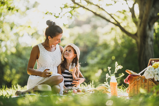 Beautiful mother and her cute daughter drinking orange juice in the park and enjoying a picnic day.
