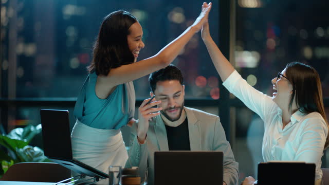 Business people, high five and laptop in success, celebration and teamwork in marketing sales and bonus at night. Professional employees excited, wow and yes for news or results on computer and bokeh