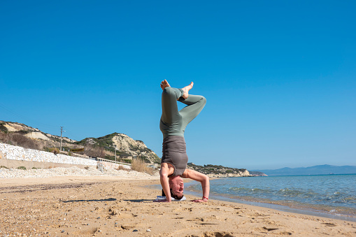Attractive middle-aged woman practicing yoga on a beautiful beach. A sunny day and a blue sky at an afternoon time.
