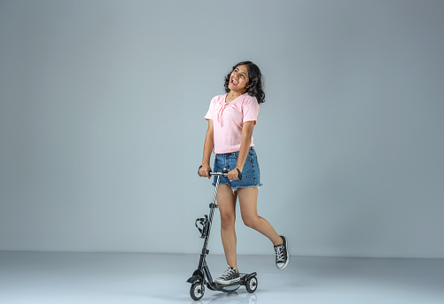 Cheerful teenage girl riding push scooter against white background
