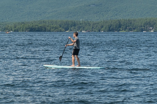 Meredith, United States – July 22, 2023: A young man enjoying a sunny day out on the water, navigating his way through the waves on a surfboard