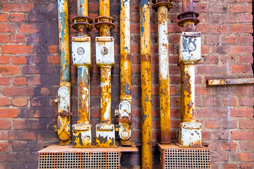 Close up view of a number of rusted and weathered industrial size pipes on wall of brick building of an old ironworks factory in Landschaftspark Duisburg, Germany