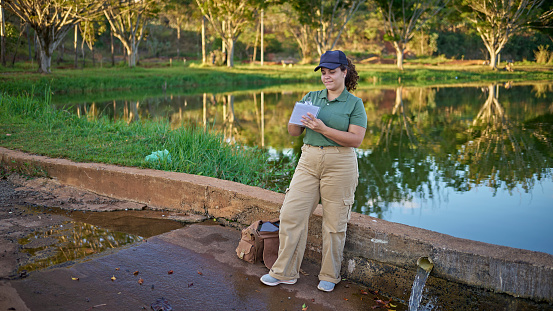Portrait of a female biologist standing in front of a lake in a natural park, writing about her examination of the environment.