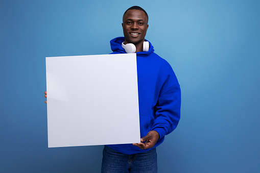25 year old young american man shows a paper poster with a mockup for advertising on the background with copy space.