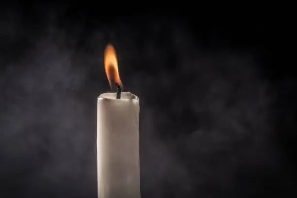 Photo of Lit white candle in a dark setting, with a plume of smoke behind it