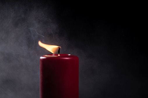 A closeup shot of a burning red candle on a black background