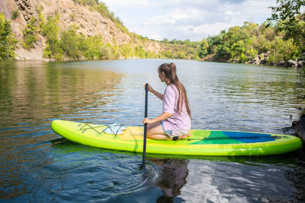 un'adolescente cavalca su una tavola sup verde su un bellissimo lago di montagna, il canyon krasnosulinsky nella regione di rostov, in russia. - paddleboard oar women lake foto e immagini stock