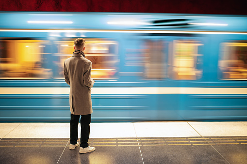 Elegant young man is standing at a metro station in Stockholm, Sweden and waiting for the train.