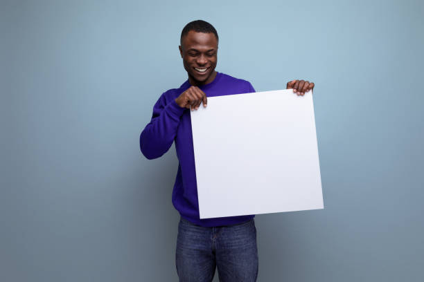 istock 30s dark-skinned American man dressed in a blue sweater shows a white board with a mock-up 1644486862