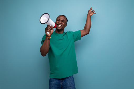 young attractive african man dressed in a basic t-shirt holding a loudspeaker to attract attention.