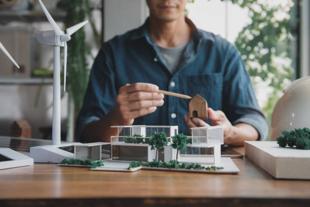 istock Architect designer making modern home office model for living using natural energy concept, natural light and green tree around, with wind turbine model and solar panels. Focus shoot at home model. 1644487854