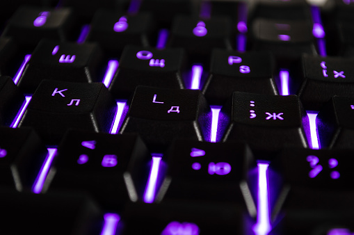 Abstract background of black computer keyboard with violet backlight. Closeup photo with bokeh, can be used like a wallpaper.