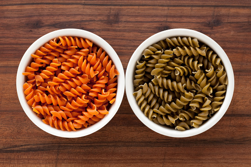 Top view of two bowls side by side with orange and green colored fusilli pasta