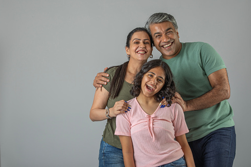 Portrait of happy loving Indian mother and father embracing daughter while standing against white background