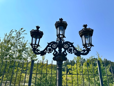 A forged black triple lantern covered in webs near the cemetery. Mystic street vintage lantern on a sunny day. Antique lamp. Garden and park lantern