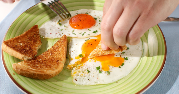 eating fried eggs with a bread on a green plate. close-up. angle view. colored background. traditional breakfast with toast . sunny day.