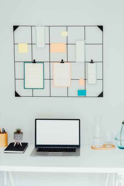 istock Modern workplace - white desk with laptop mockup empty screen, grid mood board with pinned notes and check lists for plans, office supplies at work space in home office room interior. Vertical card. 1644553107