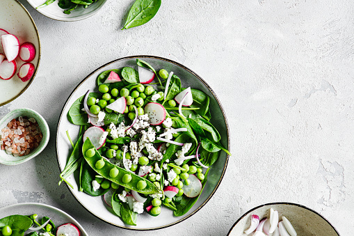 Top view of a plate of healthy green salad on white table with copy space. Healthy green salad made of chopped radish, green peas and baby spinach leaves.