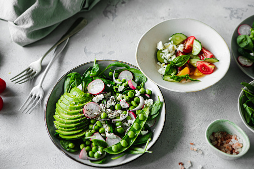 Two view of a healthy green salad plate with vegetable ingredients on the kitchen table. Summer salad made of fresh vegetables on white counter top.