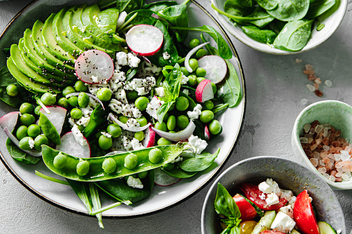 Top  view of a healthy green salad plate with ingredients. Close-up of summer salad made from chopped radishes, avocado, green peas and baby spinach leaves in the kitchen.