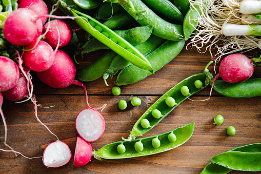 Table top view of green peas and radish on wooden table. Fresh and organic vegetable on kitchen counter.