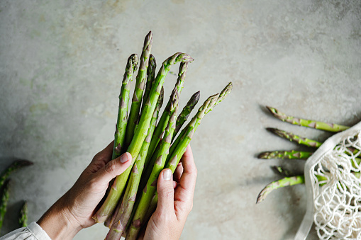 Close-up of a woman hands holding fresh asparagus. Point of view of female with organic asparagus over kitchen table.