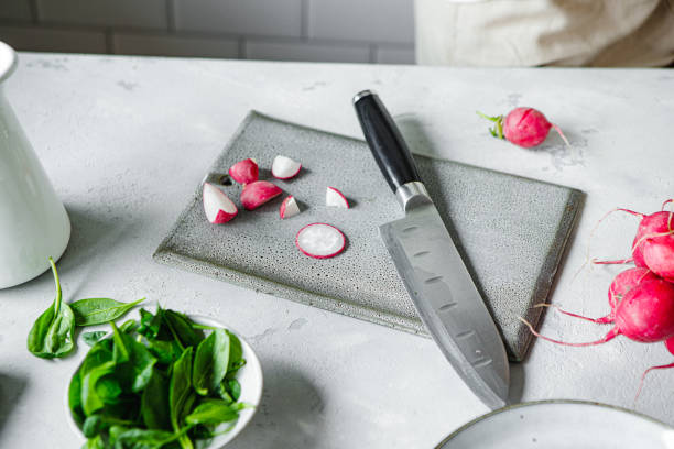 Chopped radish with a knife on chopping board over kitchen counter. Radishes, knife and cutting board on white table.