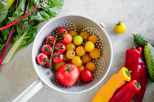 Top view of red and yellow cherry tomatoes in the colander with a variety of vegetables on the kitchen table. Different types of fresh vegetables on kitchen counter.