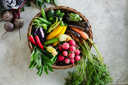 Different types of fresh vegetables in a wicker basket on white table. Basket full of mixed vegetables on a white background.