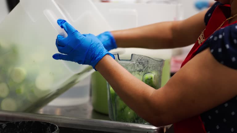 Kitchen Worker Pouring Cucumber Slices into Blender for Agua Fresca