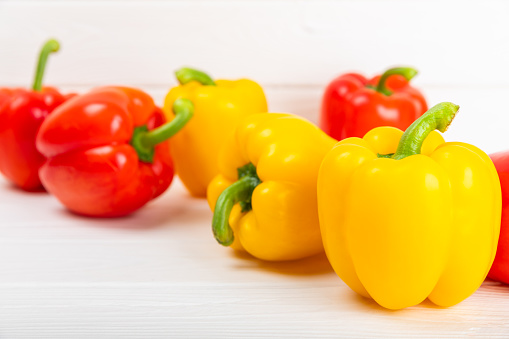 Three colorful bell peppers red yellow and green colors in a row isolated on white background with dew water drops