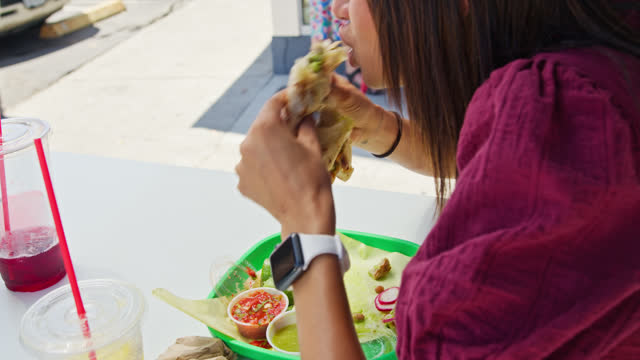 Handheld Shot of Woman Eating Chimichanga Outside Mexican Restaurant