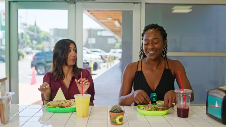 Two Friends Sit at Restaurant Counter With Dishes