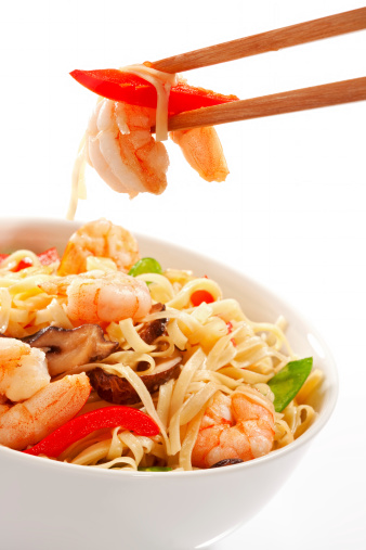 A detail of a prawn on chopsticks from stir-fried Asian noodles.