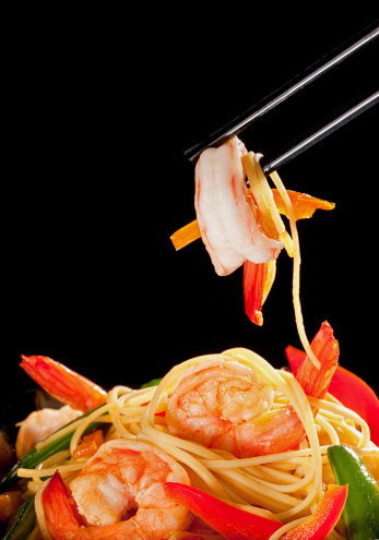 A detail of a prawn on chopsticks from stir-fried Asian noodles.