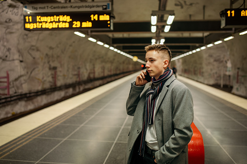 Elegant young man is standing at a metro station in Stockholm, Sweden. While waiting for the train, a teenager uses a mobile phone.