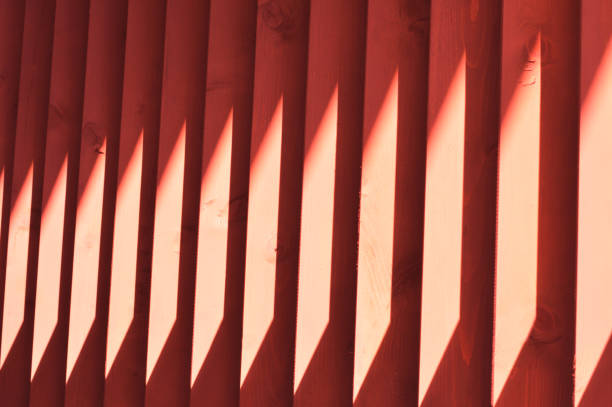 Beautiful wooden red slats. A streak of sunlight on a wooden fence. Bright abstract background. Element of finishing the facade of the building.