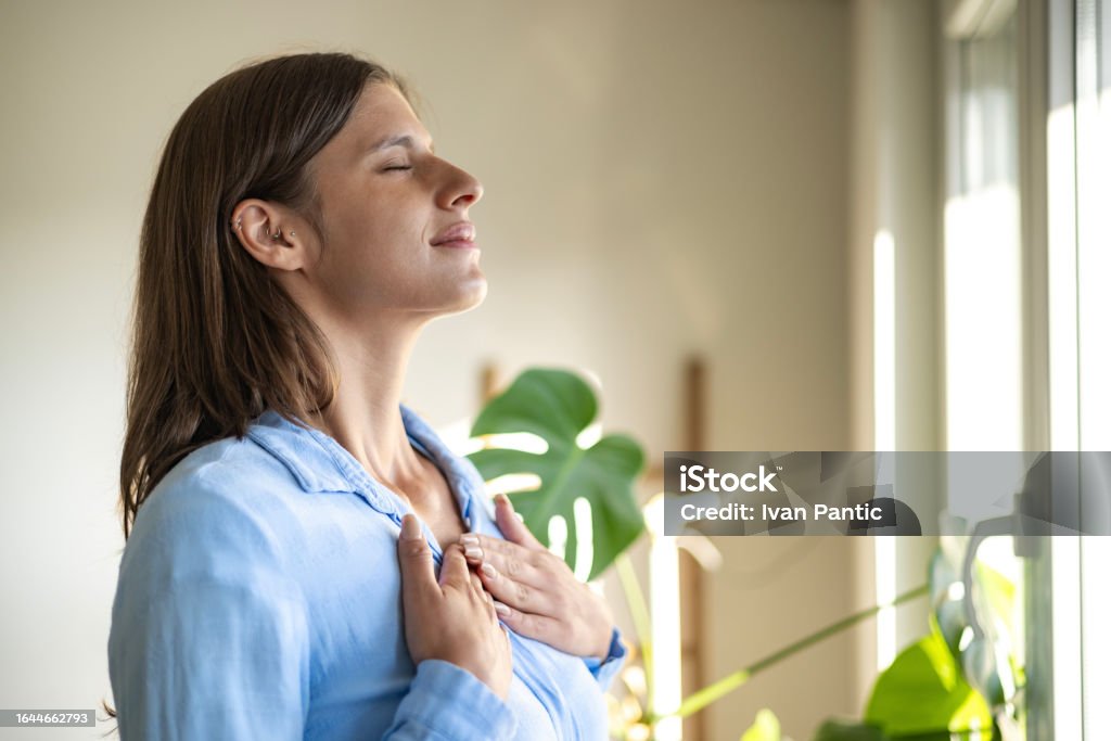 Happy woman open window drapes close eyes in delight Bathing in sunlight. An excited young lady meets the first morning at a new flat house part curtains enjoy being a homeowner. Breathing Exercise Stock Photo Happy woman open window drapes close eyes in delight Bathing in sunlight. An excited young lady meets the first morning at a new flat house part curtains enjoy being a homeowner. Breathing Exercise Stock Photo