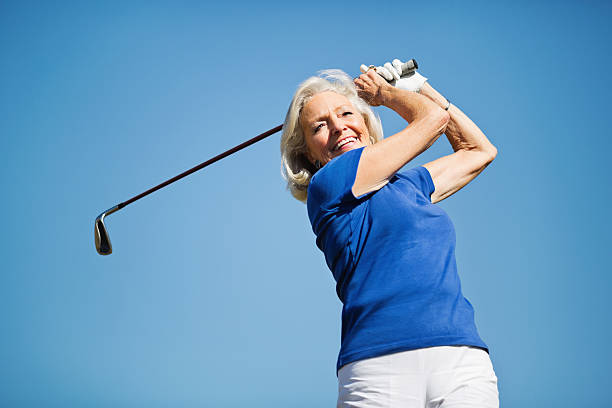 Senior Woman Swinging Golf Club Happy senior woman swinging golf club against clear sky golf glove stock pictures, royalty-free photos & images