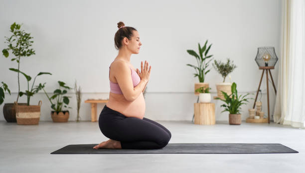 Side view portrait of young pregnant Caucasian woman doing yoga exercises and meditating in class. stock photo