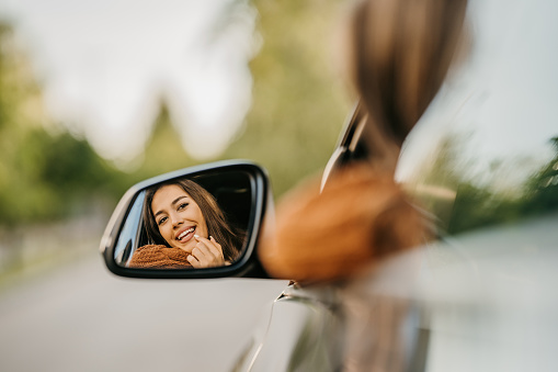 Beautiful woman looking in rear-view mirror on a car on the road.
