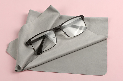 Glass cleaning grey cloth napkin with a pair of glasses over it, composition isolated on pink background. High resolution photo. Full depth of field.