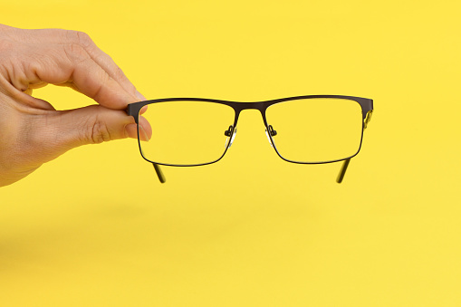 Hand holding plastic black glasses, isolated on yellow background. High resolution photo. Full depth of field.