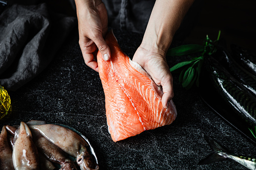 Top view of a chef preparing a fresh salmon fillet in kitchen. Close-up of male hands making a dish with raw fish.
