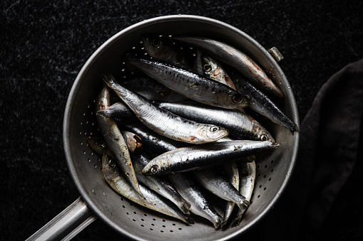 Top view of fresh raw sardines in a metal colander. Preparing seafood with sardines fishes in kitchen.
