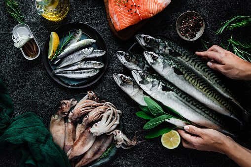 Point of view of chef hands arranging of fresh fish and seafood on black table. Fresh sardines, salmon, squid and mackerel with herbs and spices on kitchen table.