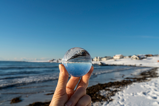 Small village at Torsfjorden fjord on island of Moskenesøya in the Lofoten archipelago in Nordland county in winter reflecting in a crystal ball in hand.