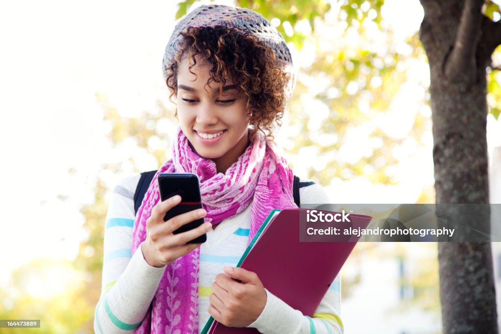 Student using a smart phone Ethnic woman with curly hair posing with a pink and fusia scarf and hat while using her cell phone and smiling. 20-29 Years Stock Photo